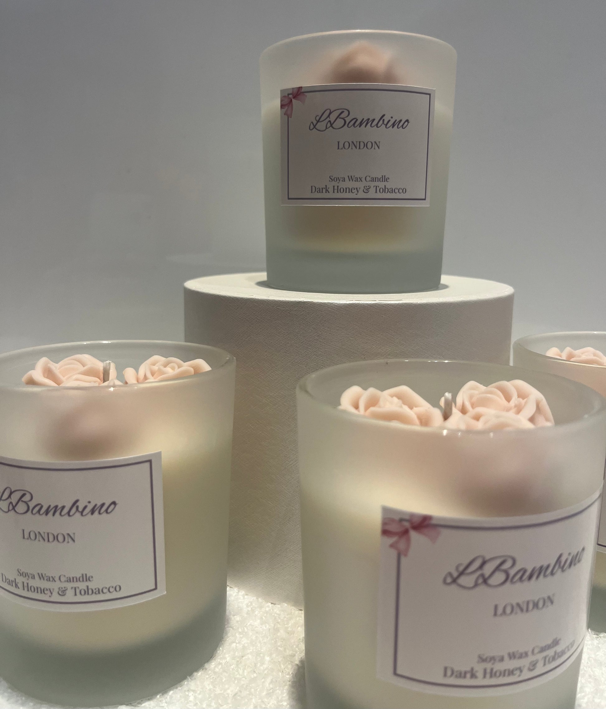 Frosted candles with floral tops and 'L Bambino London' labels on a white surface.