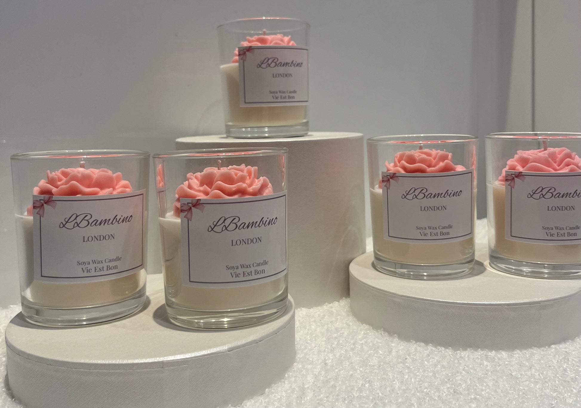 Set of candles with pink floral decorations and 'L'Bambino' labels on a white surface.