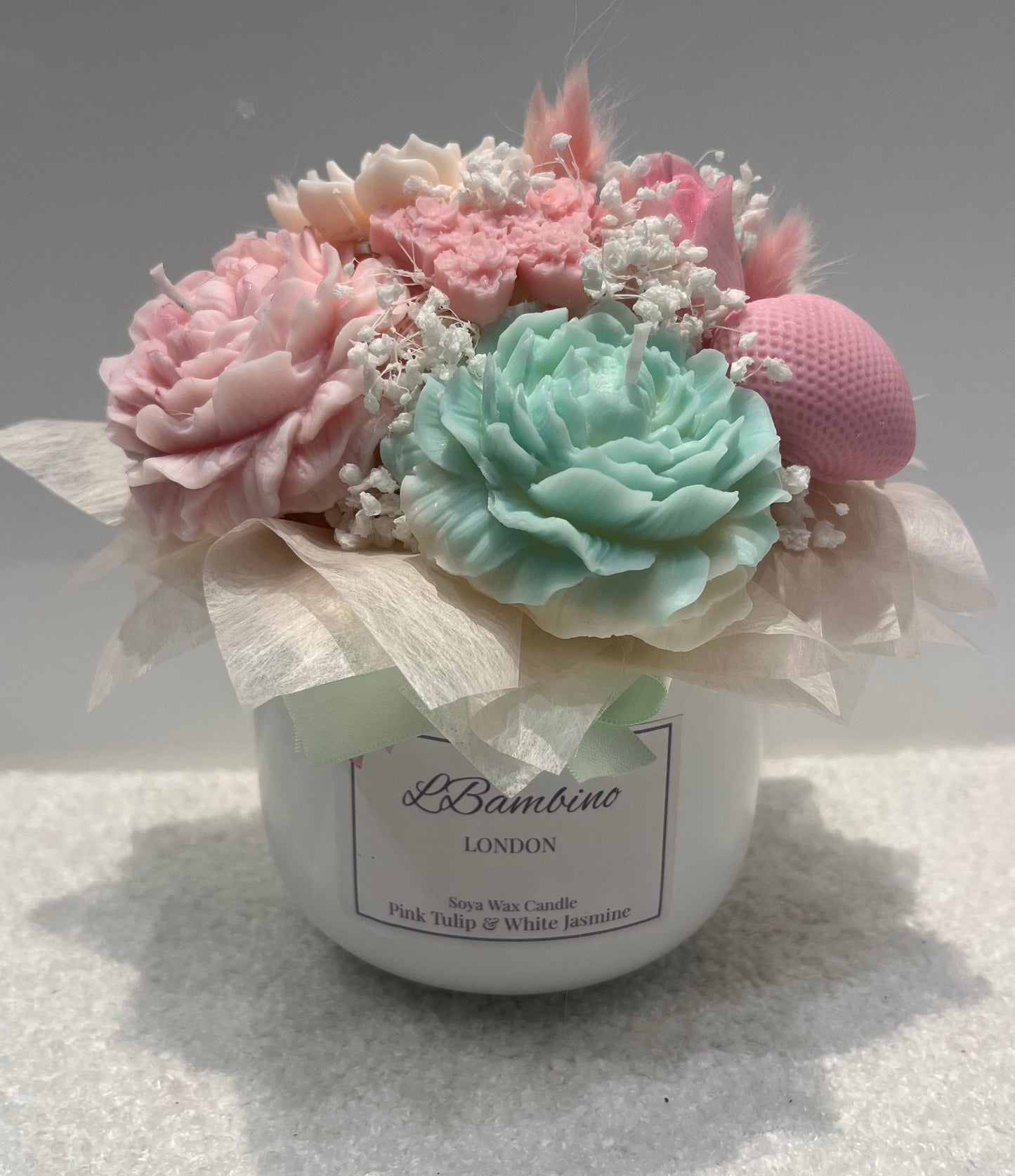 Decorative candle with pink and green flowers and a visible brand label on a light background