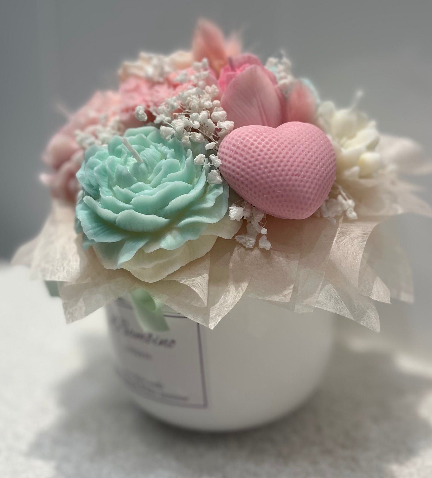 Decorative flower arrangement with pink heart and green flower in a white vase on a light background