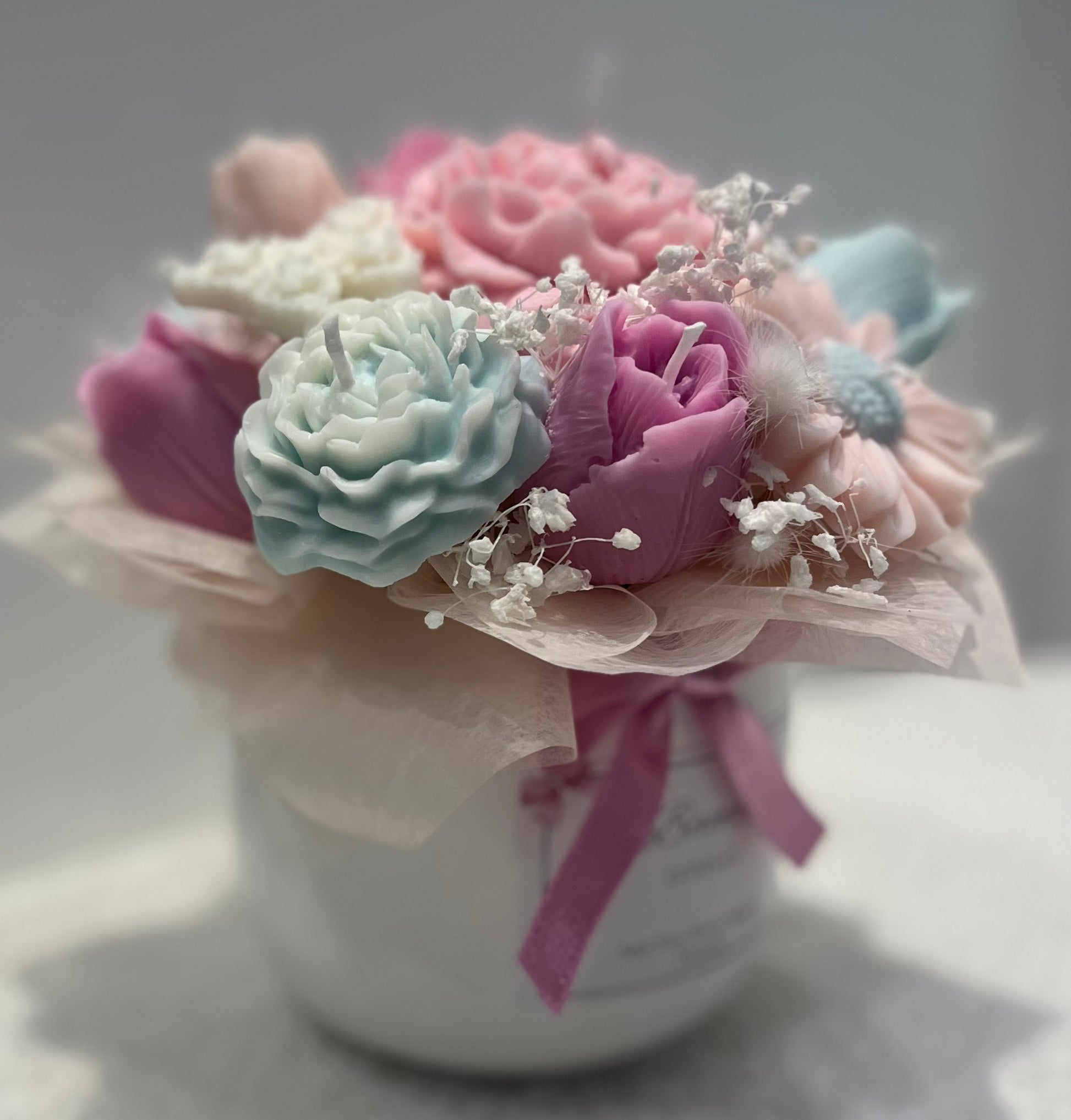Decorative flower arrangement in a white vase with a pink ribbon on a light background