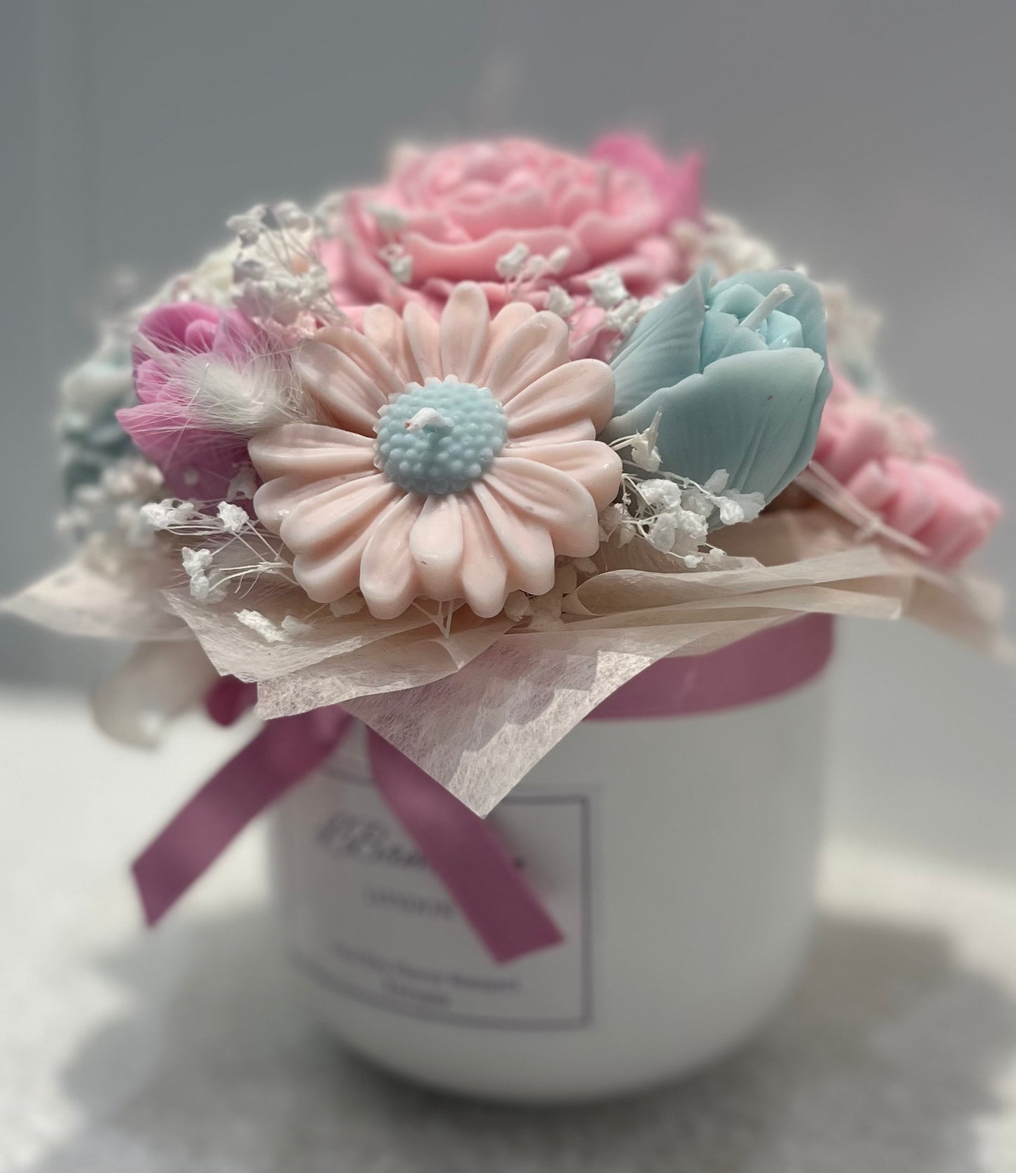 Decorative flower arrangement in a white container with a pink ribbon on a light gray background