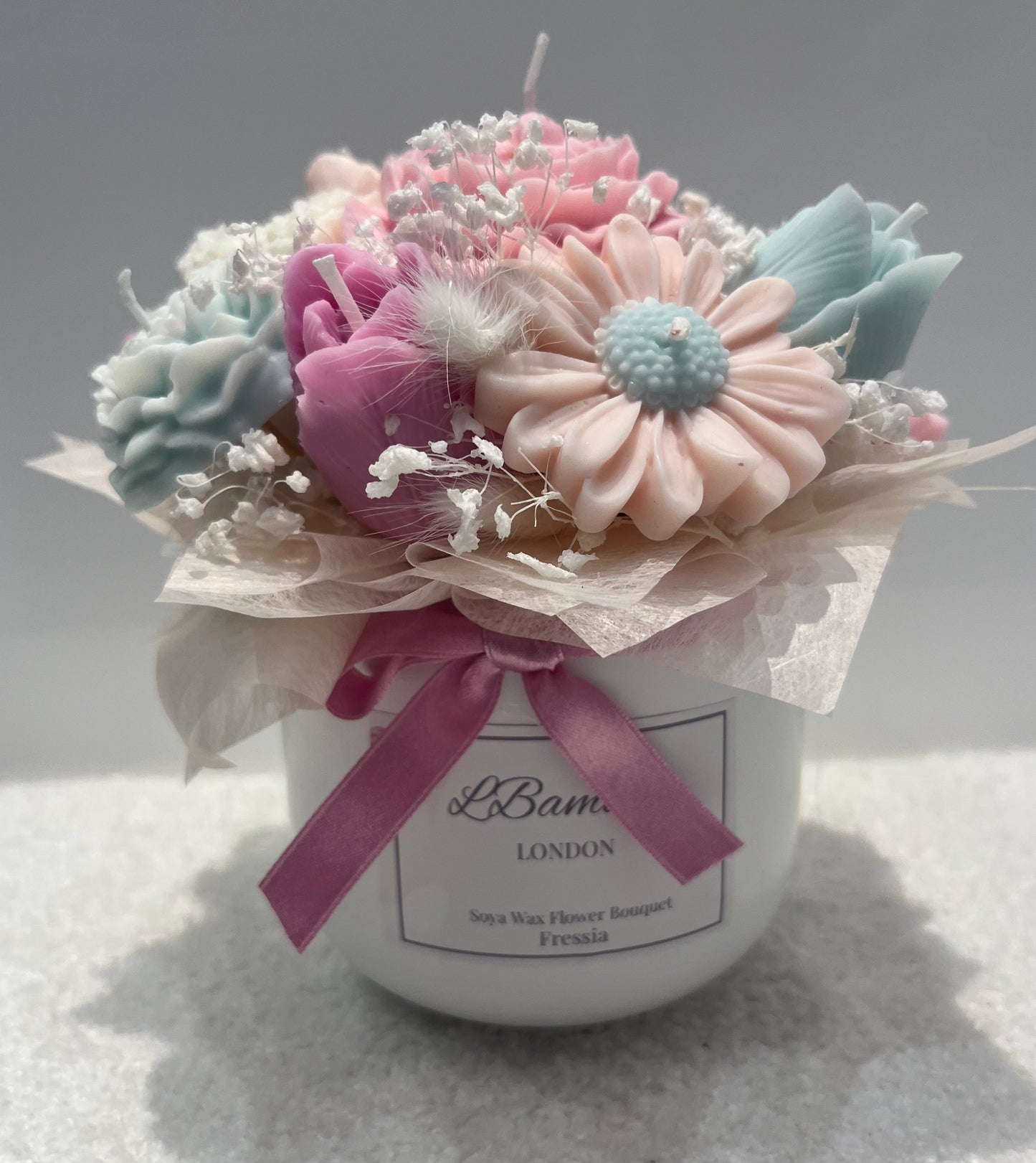 Decorative flower arrangement in a white container with a pink ribbon, branded 'Lbambino 