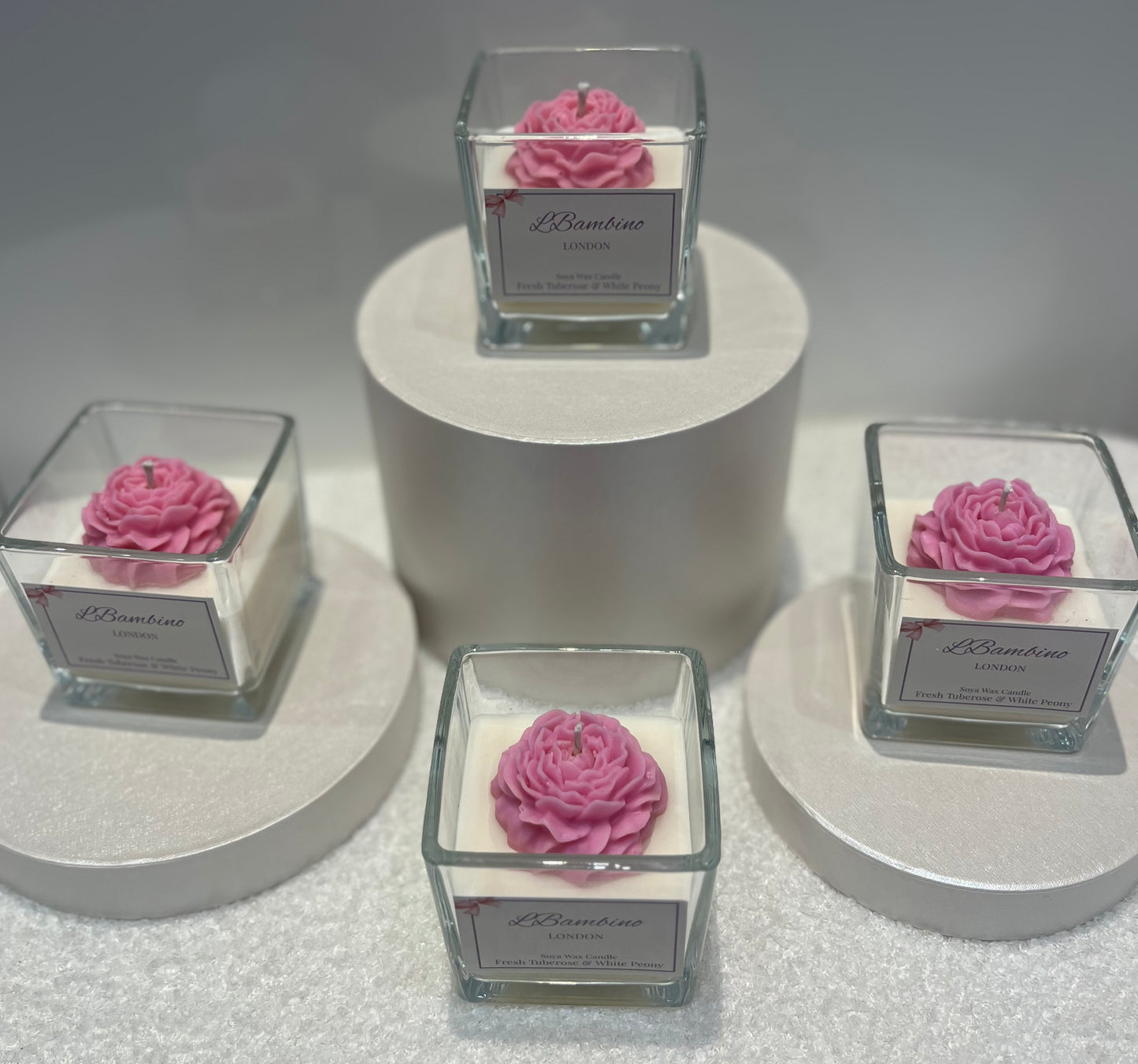 Four square glass containers with pink floral designs on a gray surface.