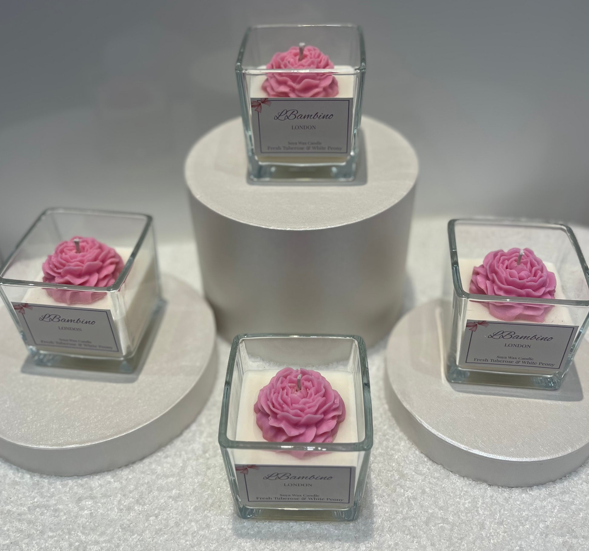Four square glass containers with pink floral designs on a gray surface.